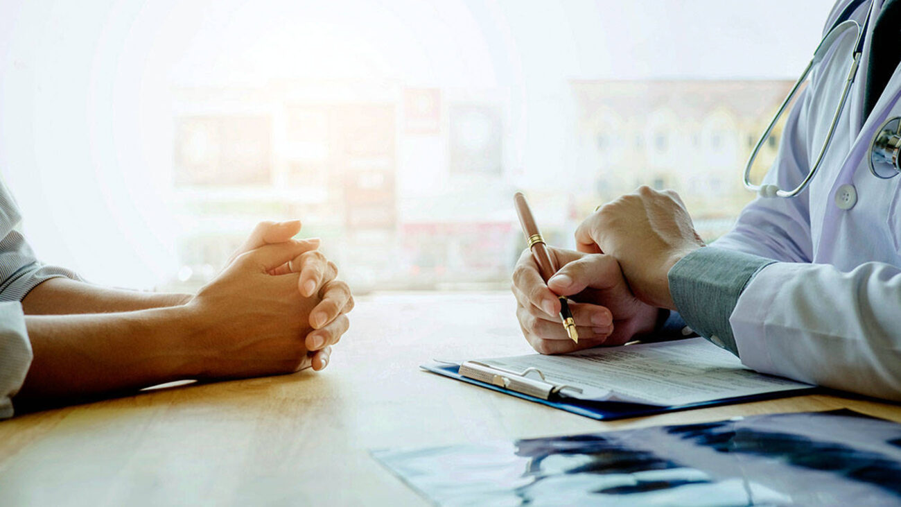 A doctor and patient face each other at a table, only their arms are showing