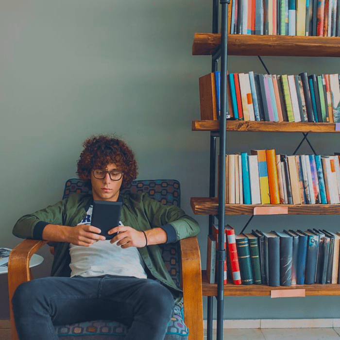 Someone sitting in a chair reading an ebook next to a bookcase