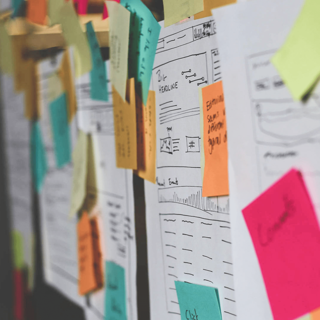 Post it notes and UX wireframes on papers taped to a glass board