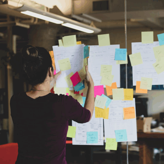 A woman collecting papers and sticky notes taped to the wall.