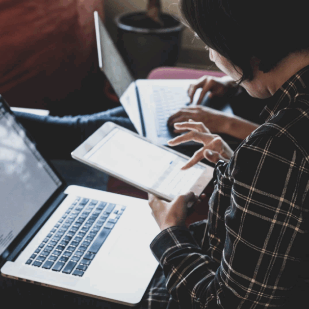 Woman using an iPad with a laptop in her lap.