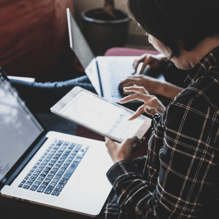 Woman using an iPad with a laptop in her lap.