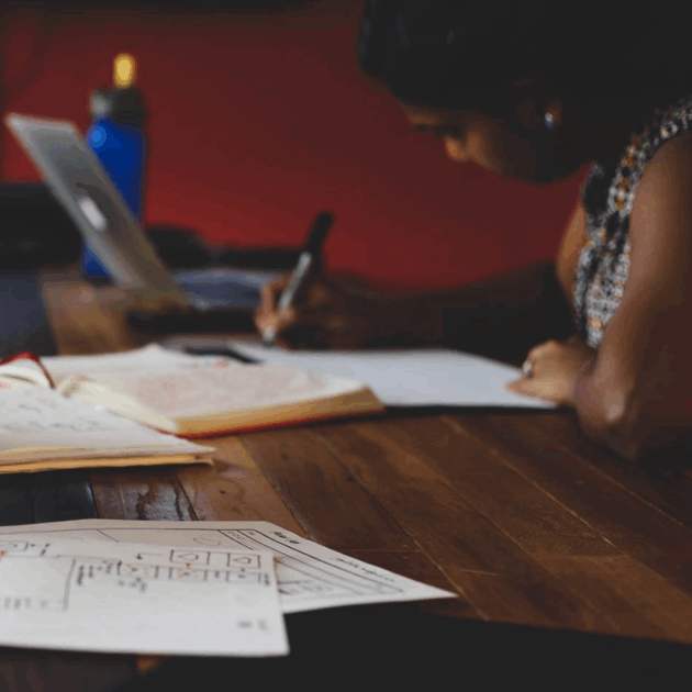 A woman drawing sketches on a piece of paper. Other sketches are laid out on the table in front of her.